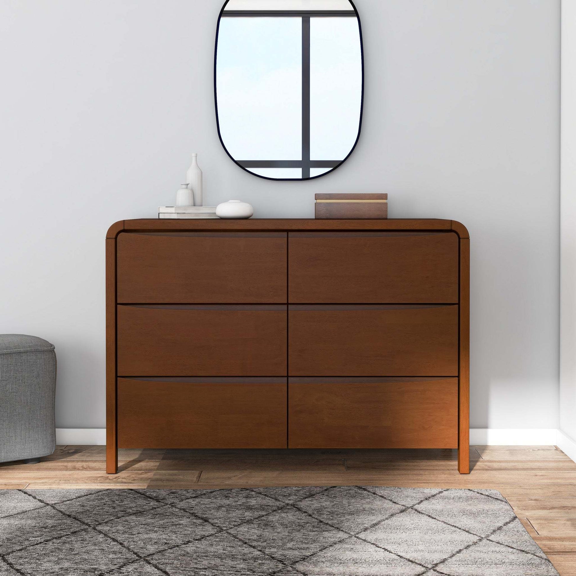 Modern wood dresser with six drawers, decorative items, mirror, and rug in bright room