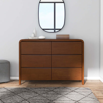Modern wood dresser with six drawers, decorative items, mirror, and rug in bright room