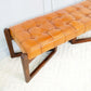 Mid-century modern tan leather bench with tufted seat and dark wood legs on white rug