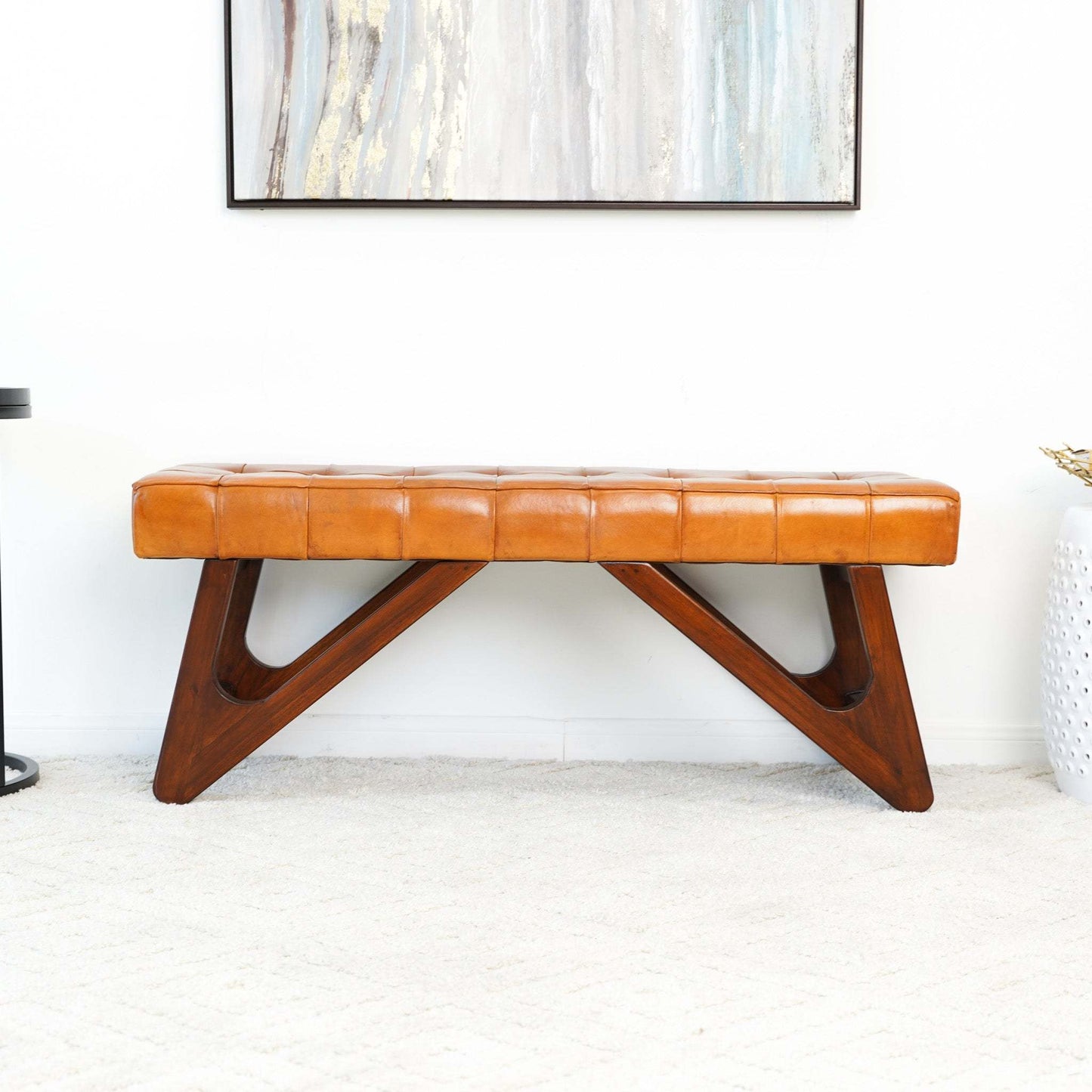 Mid-century modern tan leather bench with geometric wooden legs in a bright living room