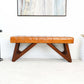 Mid-century modern tan leather bench with geometric wooden legs in a bright living room