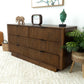 Modern wood dresser with six drawers, decorative accents, and indoor plant in a home setting