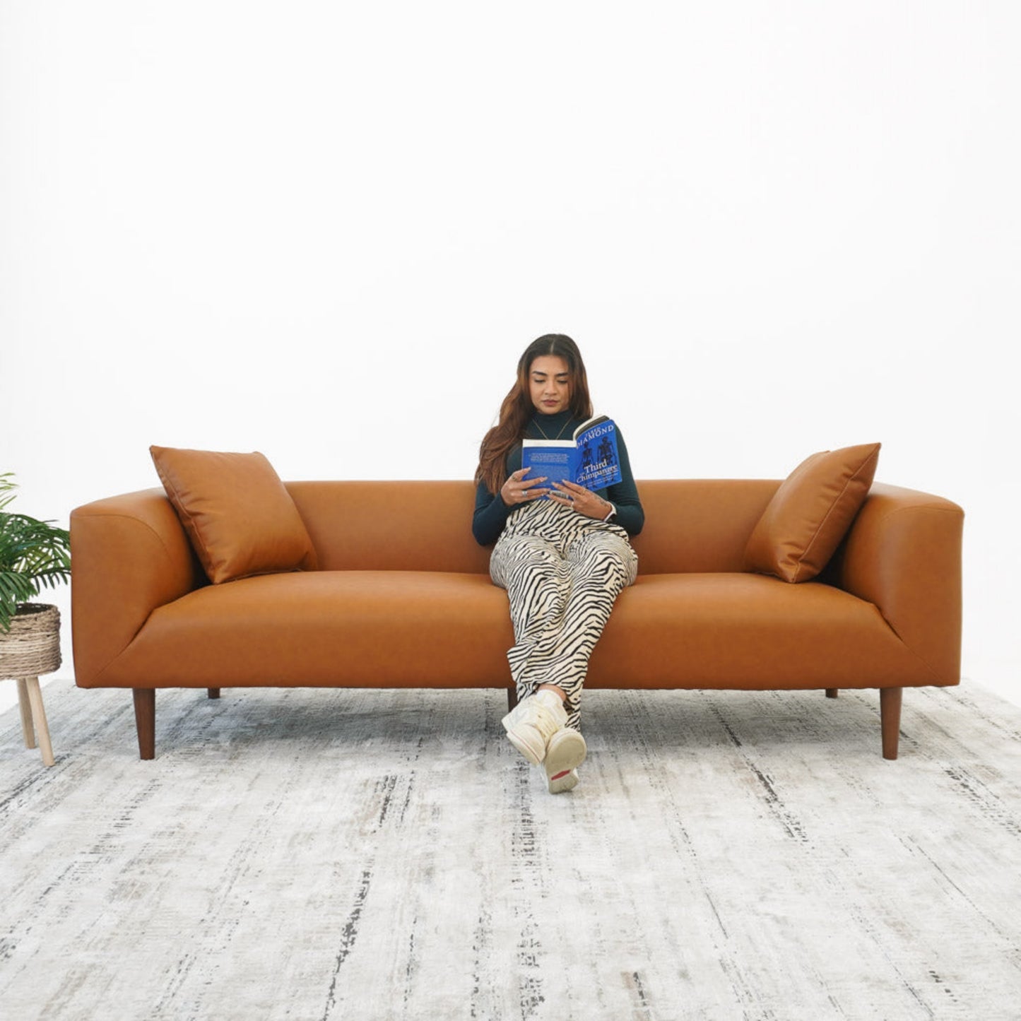 Woman reading on modern brown leather sofa with pillows, FredCo International furniture