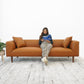 Woman reading on modern brown leather sofa with pillows, FredCo International furniture