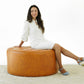 Woman in white dress sitting on large round tan leather ottoman, modern home furniture setting.