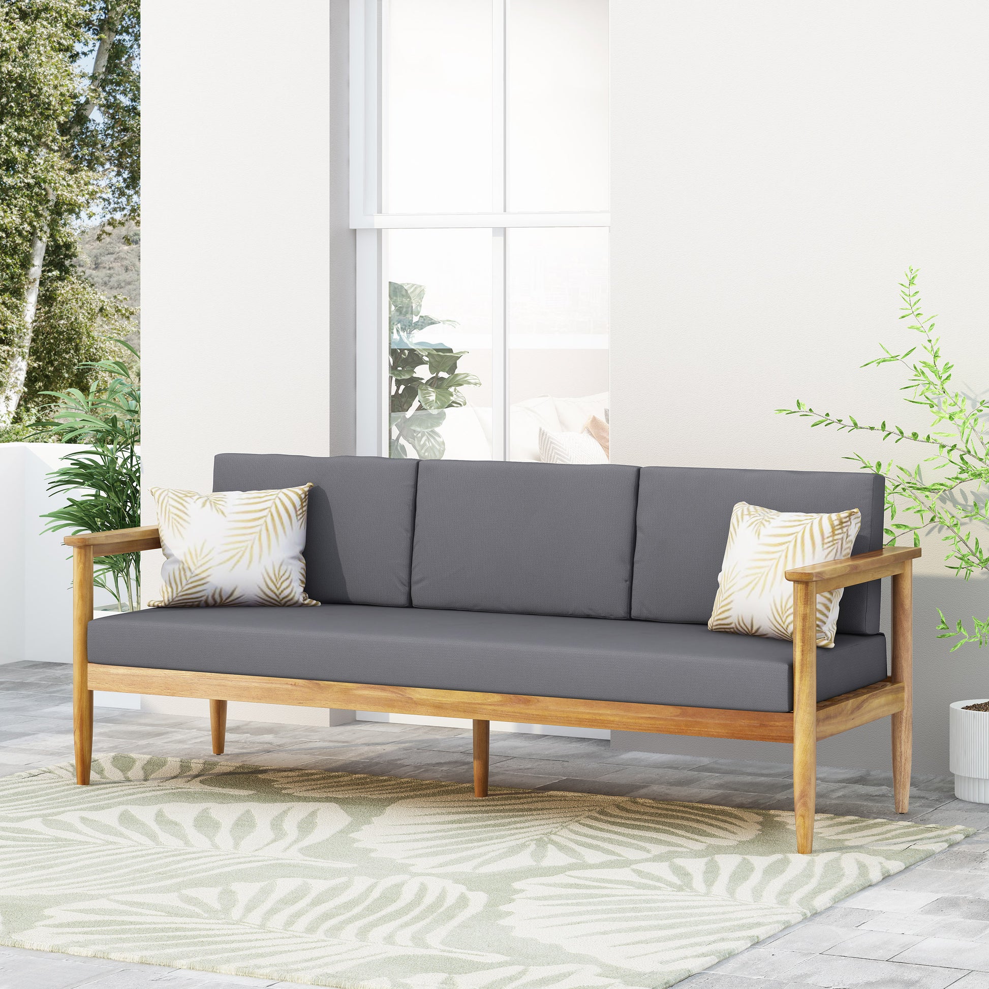 Modern wooden sofa with gray cushions and tropical pillows on patio, FredCo International furniture