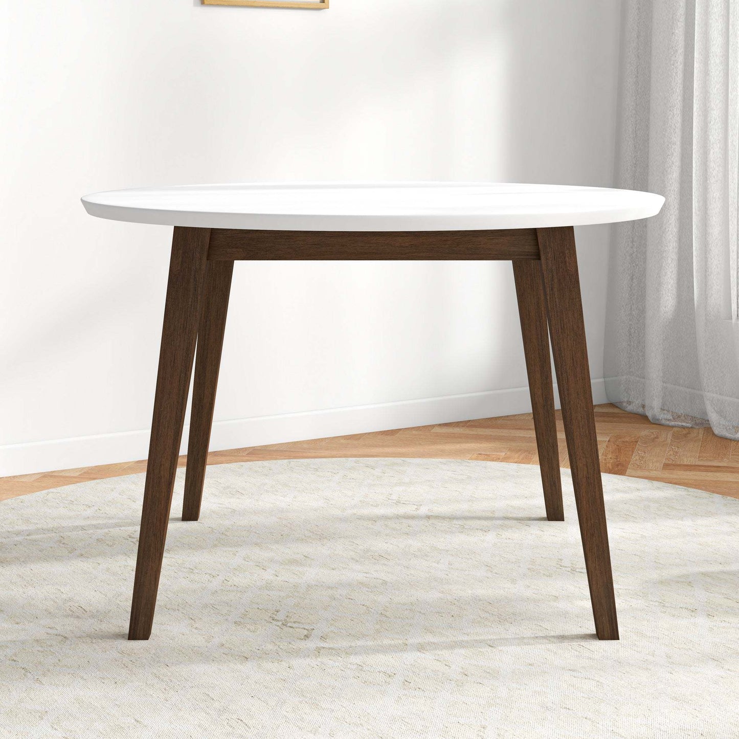 Modern round dining table with white top and dark wood legs in a bright home interior