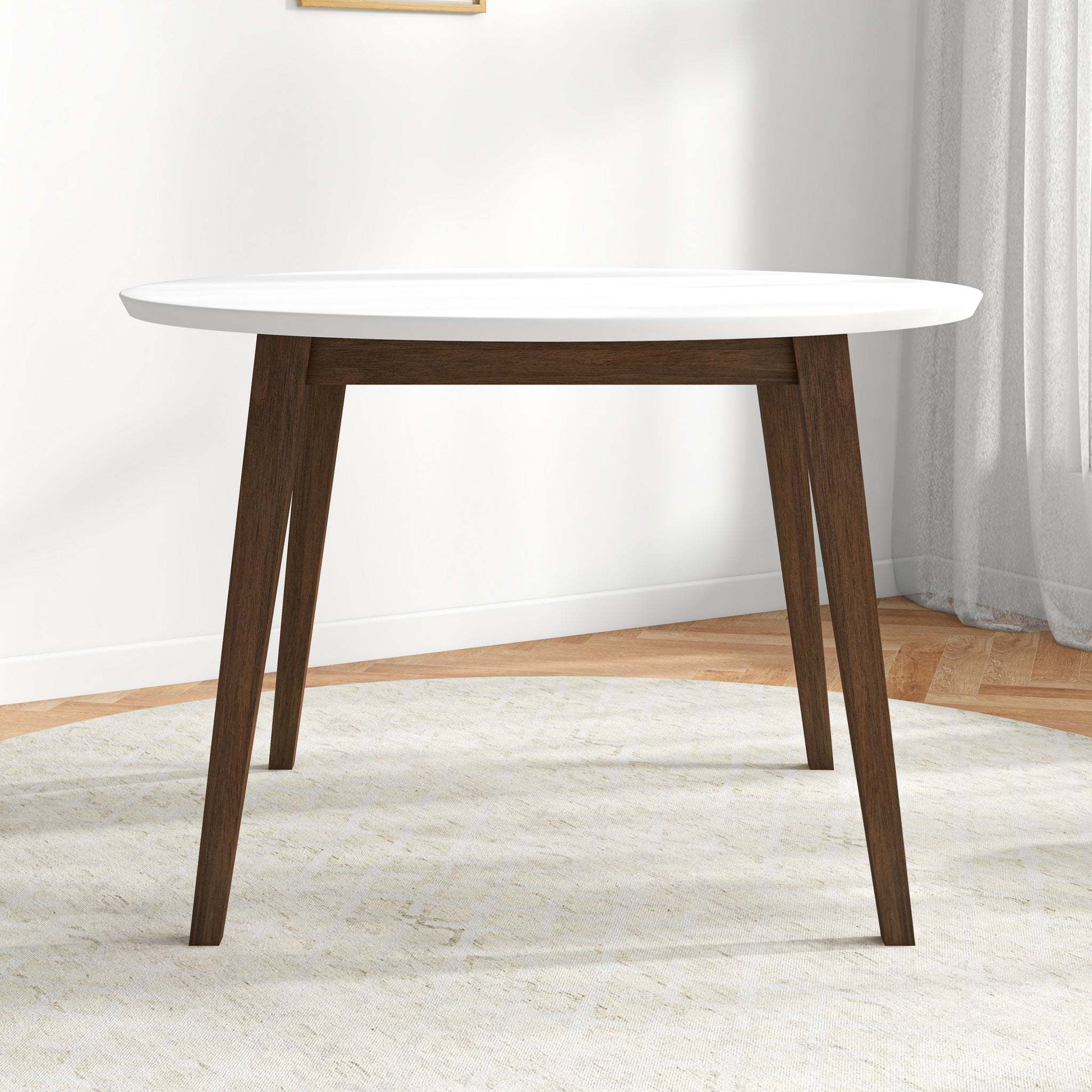 Modern round dining table with white top and dark wood legs in a bright home interior