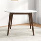 Modern round dining table with white top and dark wood legs in a bright home interior