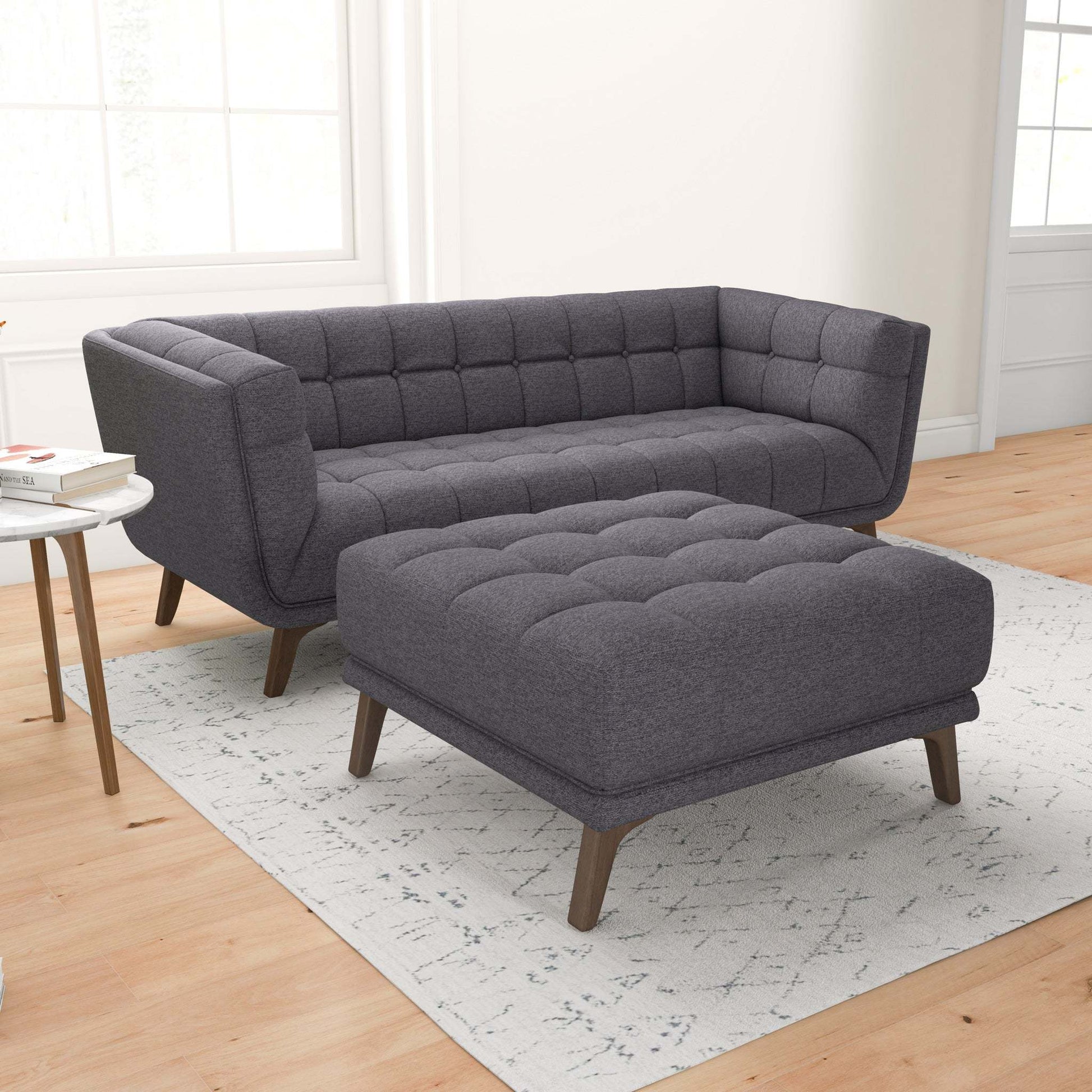 Modern tufted dark gray sofa and ottoman set on light rug in bright living room