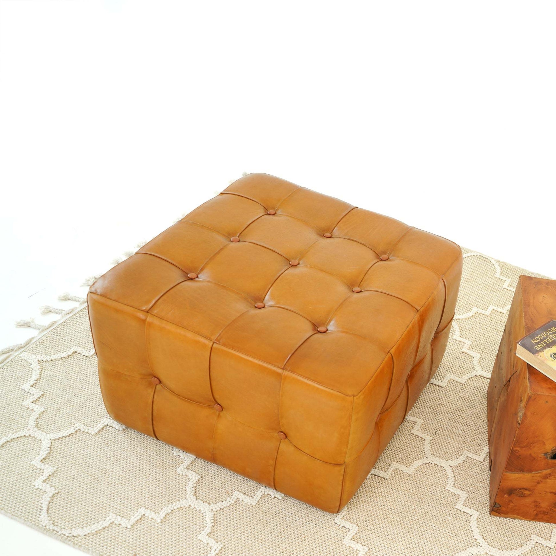 Square tufted leather ottoman on beige patterned rug, modern home furniture from FredCo International