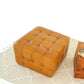 Square tufted leather ottoman on beige patterned rug, modern home furniture from FredCo International