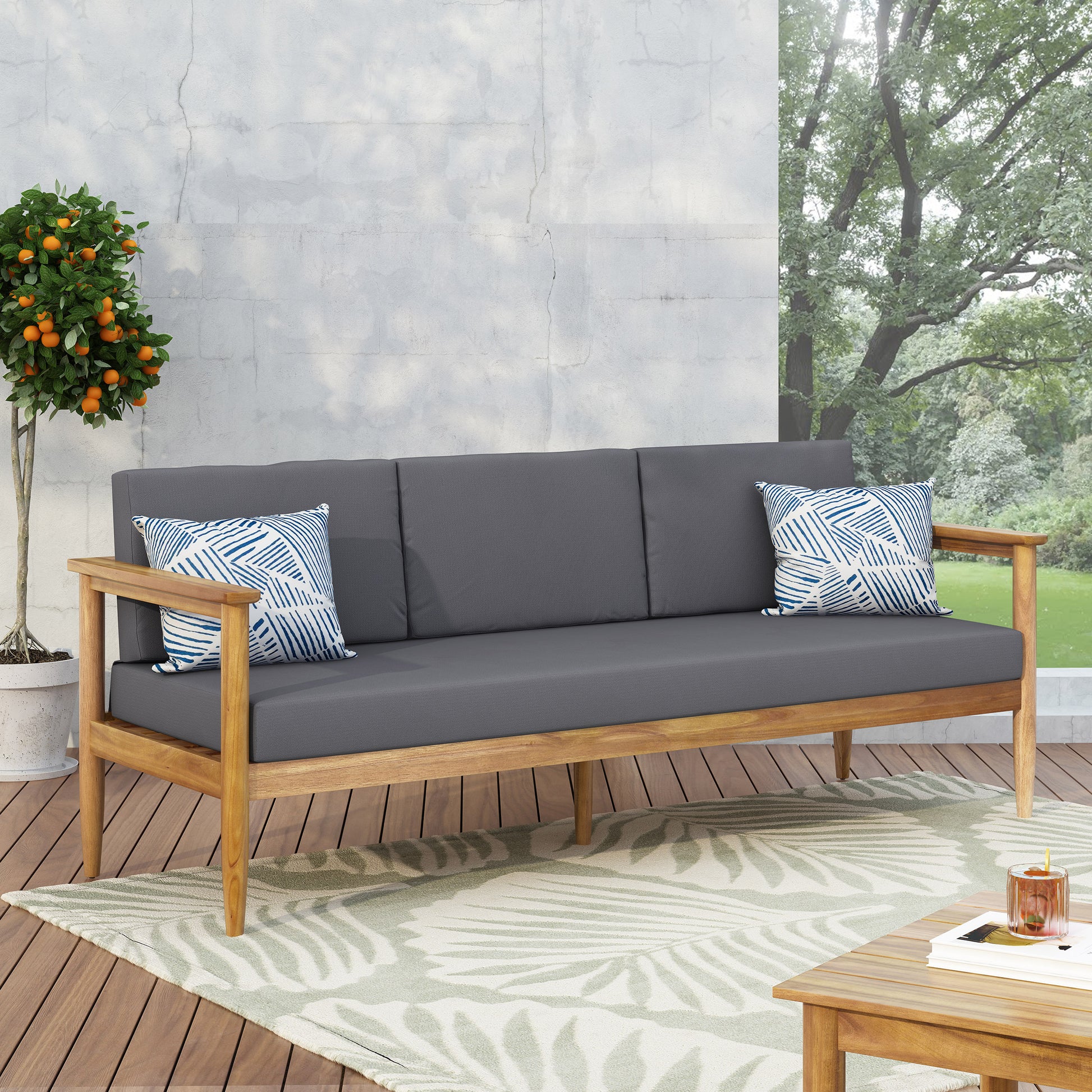 Modern wooden outdoor sofa with dark gray cushions, accent pillows, on patio at FredCo International
