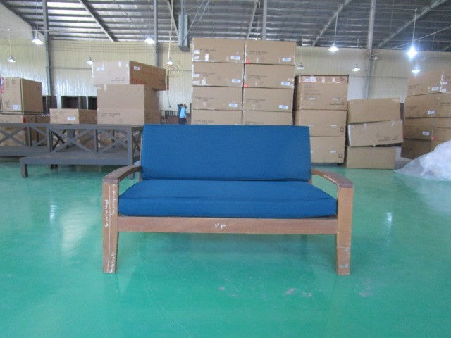 Blue cushioned wooden sofa displayed in warehouse with stacked shipping boxes