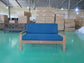 Blue cushioned wooden sofa displayed in warehouse with stacked shipping boxes